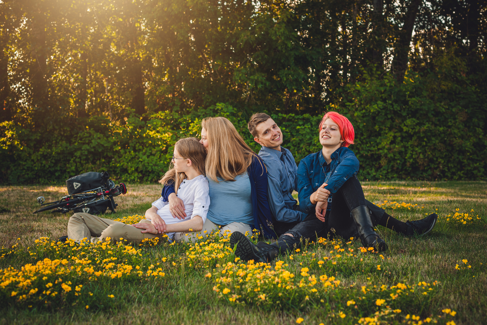 A family with two teens relaxes on the grass, surrounded by butterups. Thier bikes in the background on a beautiful spring evening.