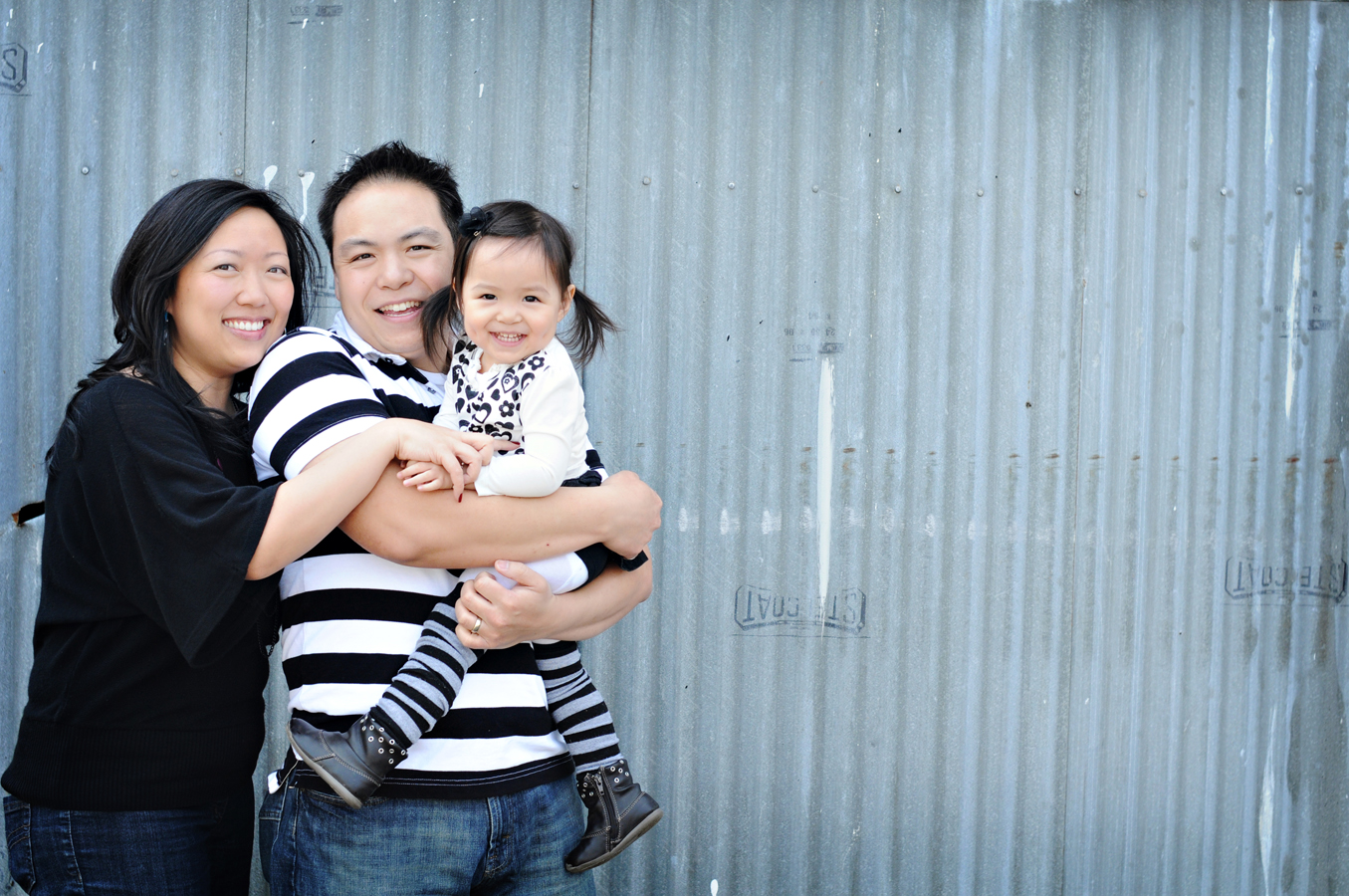 A family of three in Steveston, Richmond. All dressed in black and white dad holding his toddler daughter and all smiling at the camera.