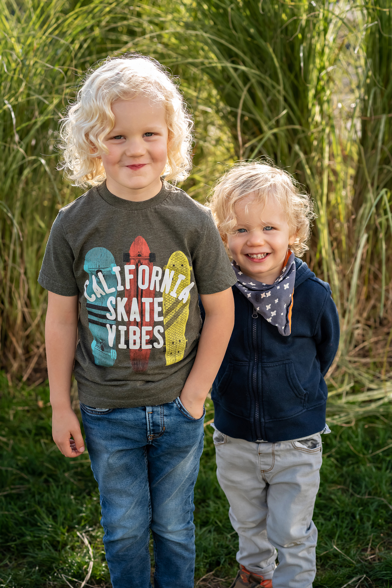 Blonde hair brothers stand in front of long backlit grass together. 